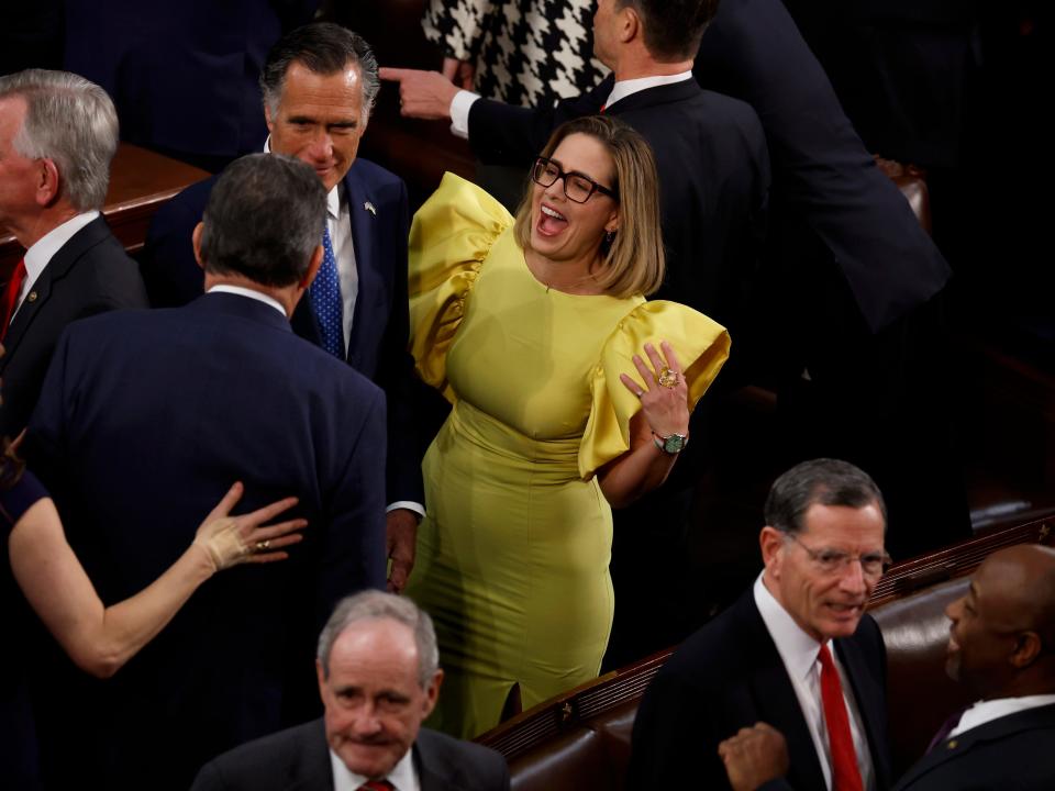 U.S. Sen. Kyrsten Sinema (I-AZ) (R) talks to fellow members of Congress including Sen. Mitt Romney (R-UT) (C) during U.S. President Joe Biden's State of the Union address during a joint meeting of Congress in the House Chamber of the U.S. Capitol on February 07, 2023 in Washington, DC.