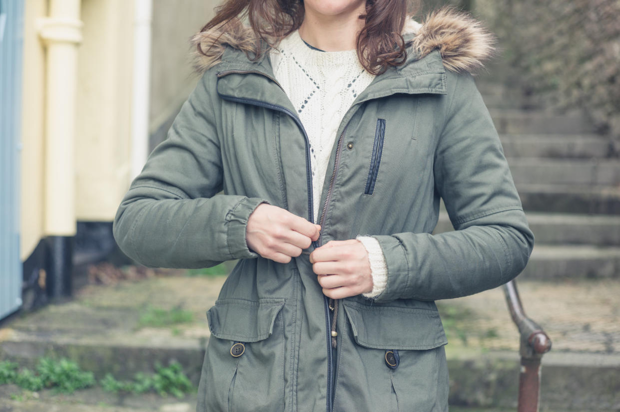 A young woman is standing outside and is buttoning her coat