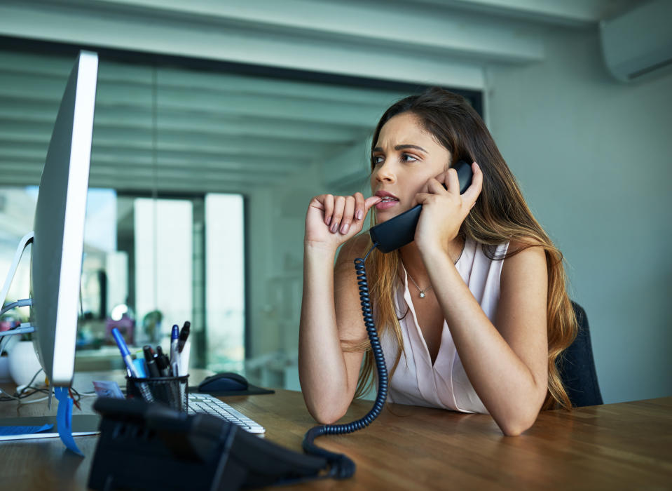 Shot of a young businesswoman biting her nails while talking on a phone in an office