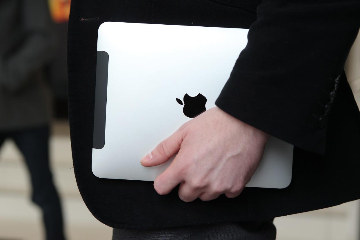 A silver Apple iPad being carried by a person wearing a black blazer