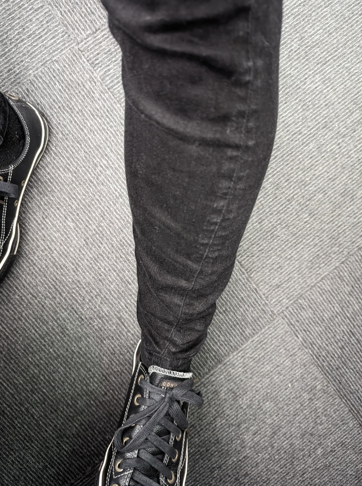 Photo of a person's leg wearing jeans and a black sneaker, viewed from above