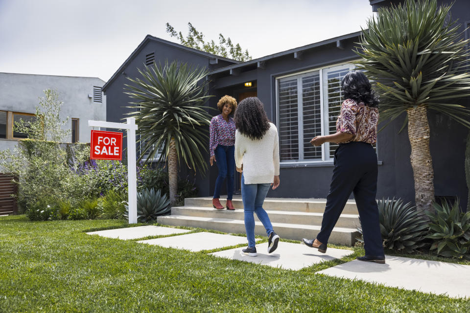 Three individuals exploring the exterior of a home with a "For Sale" sign