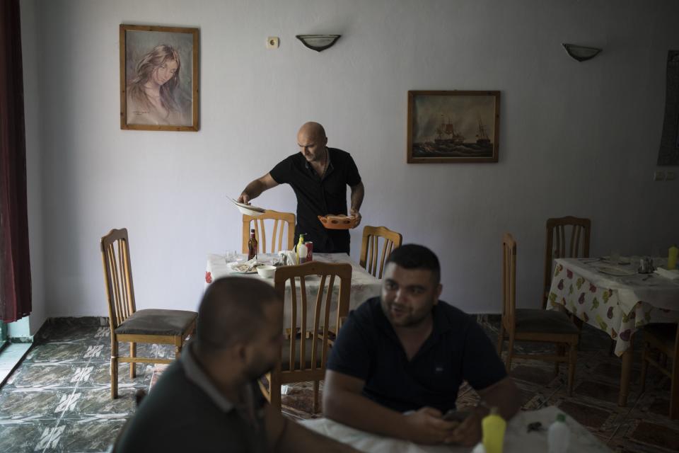 Un camarero recoge una mesa en un restaurante de Ballsh mientras dos clientes charlan en otra. (Foto: Daniel Cole / AP).