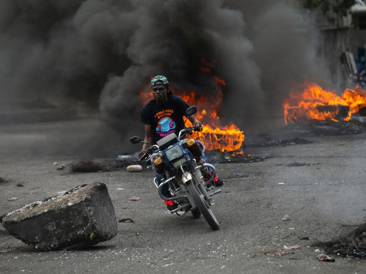 A moto-taxi driver rides past a burning barricade set up by demonstrators to protest against fuel price hikes and to demand that Haitian Prime Minister Ariel Henry step down, in Port-au-Prince, Haiti, on Sept. 26, 2022. (Odelyn Joseph/The Associated Press - image credit)