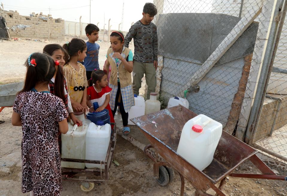 An Iraqi displaced man and little girls collect water from a donated tank at Al-Amiriya camp for refugees, 95 km western Baghdad, Iraq, 15 May 2022 (EPA)