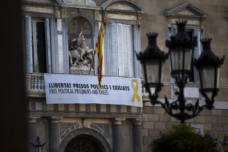 A banner reading "Free Political Prisoners and Exiles" and with a yellow ribbon, hangs at the headquarter of the Government and the Presidency of Catalonia in Barcelona, Spain, Wednesday, March 20, 2019. A dispute between Spanish authorities and Catalan separatists over a yellow ribbon symbol is building into a hot issue ahead of Spain's general election next month. (AP Photo/Emilio Morenatti)