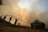 A firefighter tries to extinguish a fire as volunteers hold the water hose during a wildfire in Agios Stefanos, in northern Athens, Greece, Friday, Aug. 6, 2021. Thousands of people have fled wildfires burning out of control in Greece and Turkey, including a major blaze just north of the Greek capital of Athens that left one person dead. (AP Photo/Petros Karadjias)