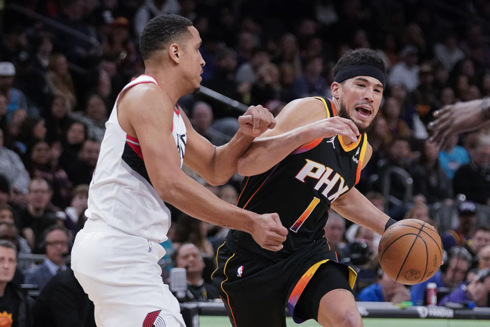 Phoenix Suns' Devin Booker (1) works his way around Portland Trail Blazers' Malcolm Brogdon during the first half of an NBA basketball game in Phoenix, Monday, Jan. 1, 2024. (AP Photo/Darryl Webb)