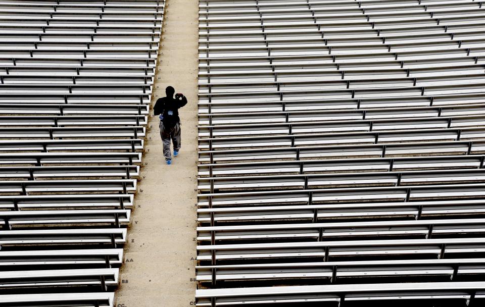 FILE - In this July 16, 2014, file photo, a student walks through empty seats inside Kenan Stadium at the University of North Carolina in Chapel Hill, N.C., where preparations continue for the upcoming college football season. The crippling grip the coronavirus pandemic has had on the sports world has forced universities, leagues and franchises to evaluate how they might someday welcome back fans. (AP Photo/Gerry Broome, File)