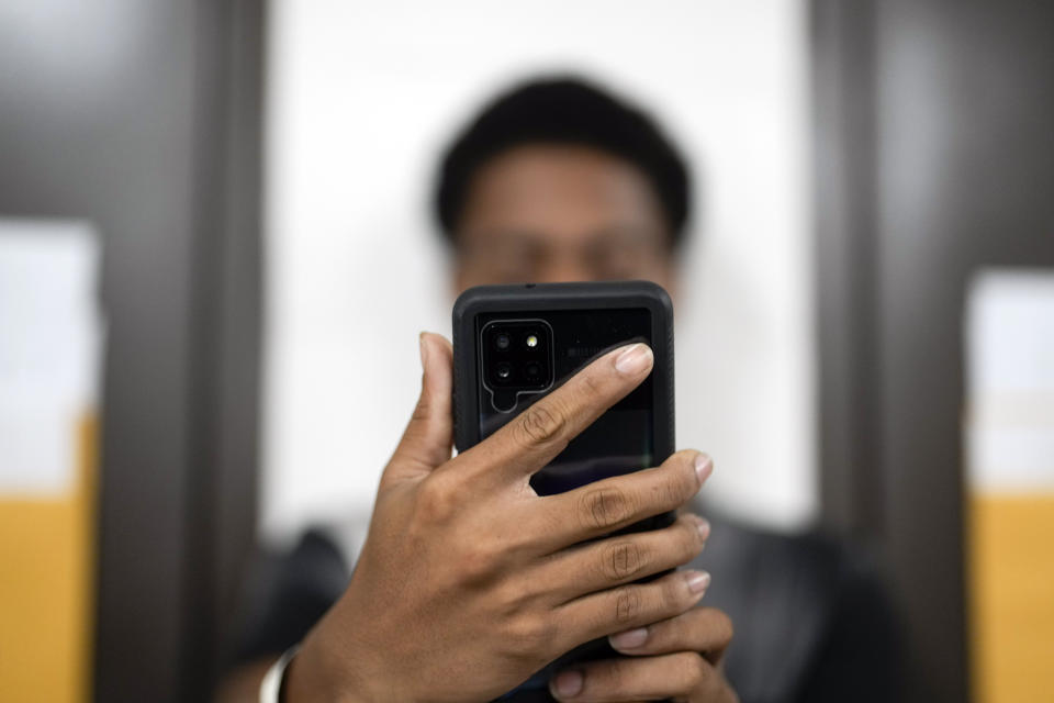 FILE - A man takes a picture of himself using a phone that will be used to track him once he leaves an immigration and customs processing facility on March 15, 2023, in San Diego. U.S. authorities are sharply expanding the reach of curfews for the heads of asylum-seeking families while they wait for initial screenings after crossing the border, signaling they are comfortable with early results of what is intended as an alternative to detention. (AP Photo/Gregory Bull, File)