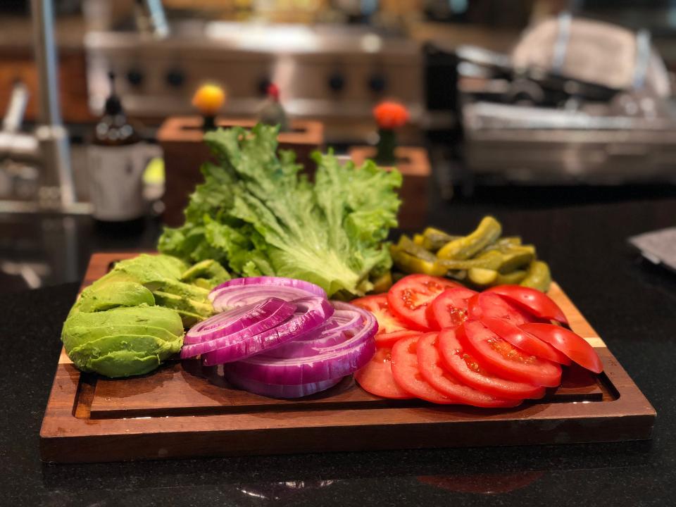 Fresh toppings for burger including lettuce, guacamole, onions, tomatoes and pickles.