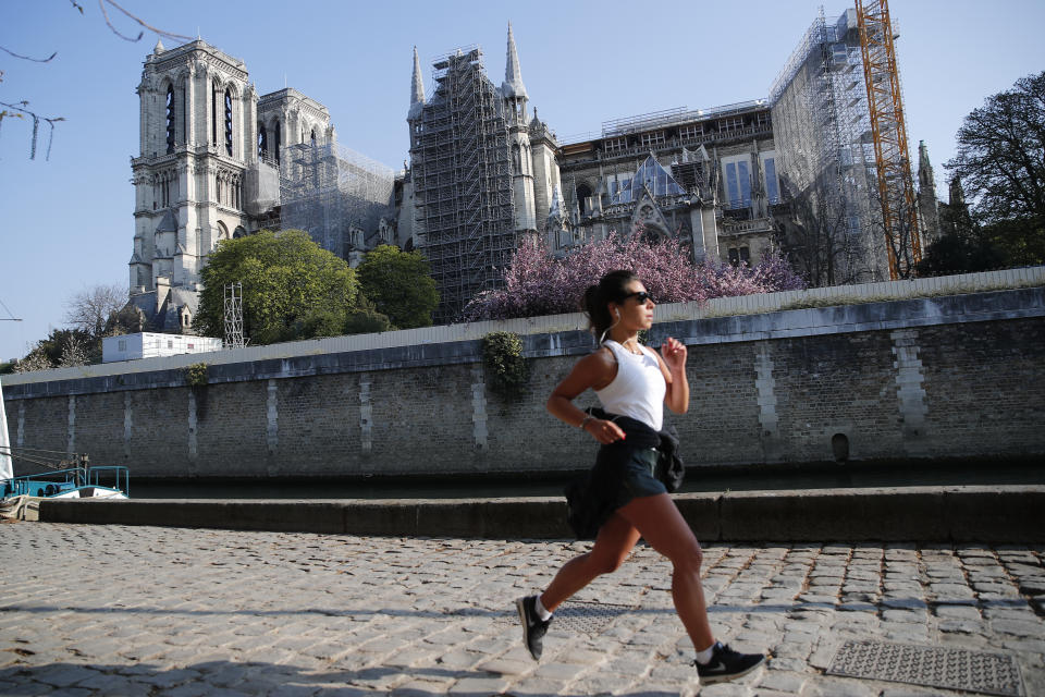 A woman jogs in front of Notre Dame cathedral, Thursday, April 15, 2021 in Paris. Two years after a fire tore through Paris' most famous cathedral and shocked the world, French President Emmanuel Macron is visiting the building site that Notre Dame has become to show that French heritage has not been forgotten despite the coronavirus. (AP Photo/Francois Mori)