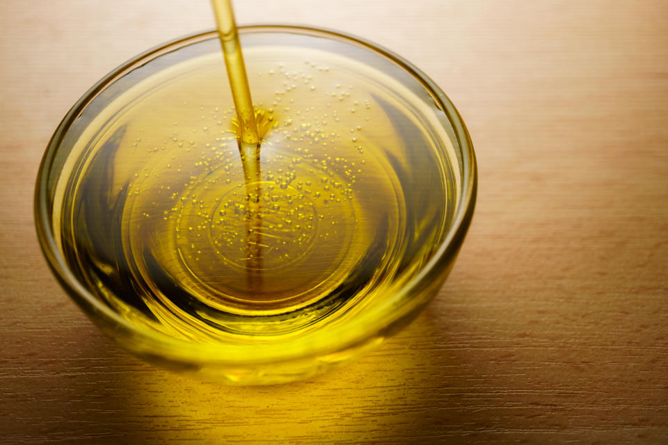 Oil being poured into a clear bowl on a wooden surface