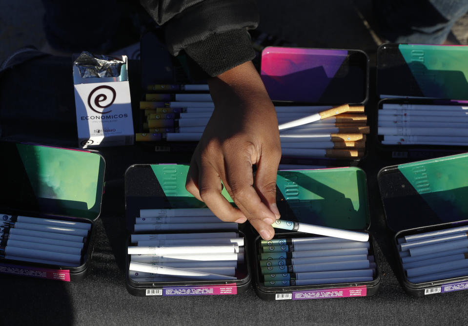 In this Dec. 2, 2018 photo, Honduran migrant Juan Carlos Garcia, 16, sells a range of flavored and regular cigarettes inside the former concert venue Barretal, now serving as a shelter for more than 2,000 migrants in Tijuana, Mexico. Facing the possibility of a months-long wait in Tijuana before even having an opportunity to request asylum in the United States, members of the migrant caravans that have arrived in Tijuana are looking for work. Some are creating their own informal businesses. (AP Photo/Rebecca Blackwell)