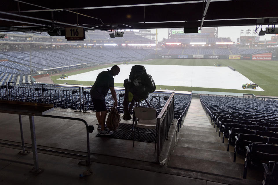 A technician covers a TV camera after the the Miami Marlins versus he Philadelphia Phillies baseball game was called due to rain on Thursday, July 1, 2021, in Philadelphia. (AP Photo/Laurence Kesterson)