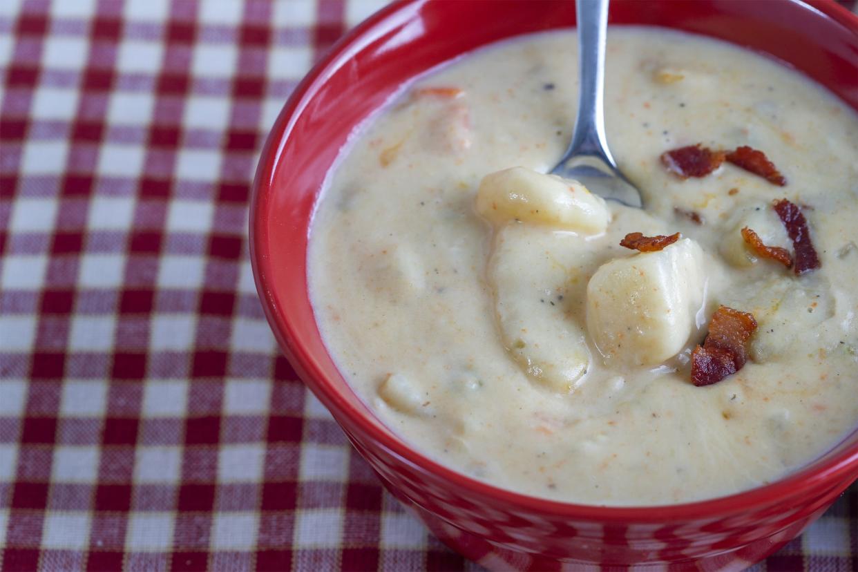 A spoon in potato soup in a red bowl on a red checkered tablecloth