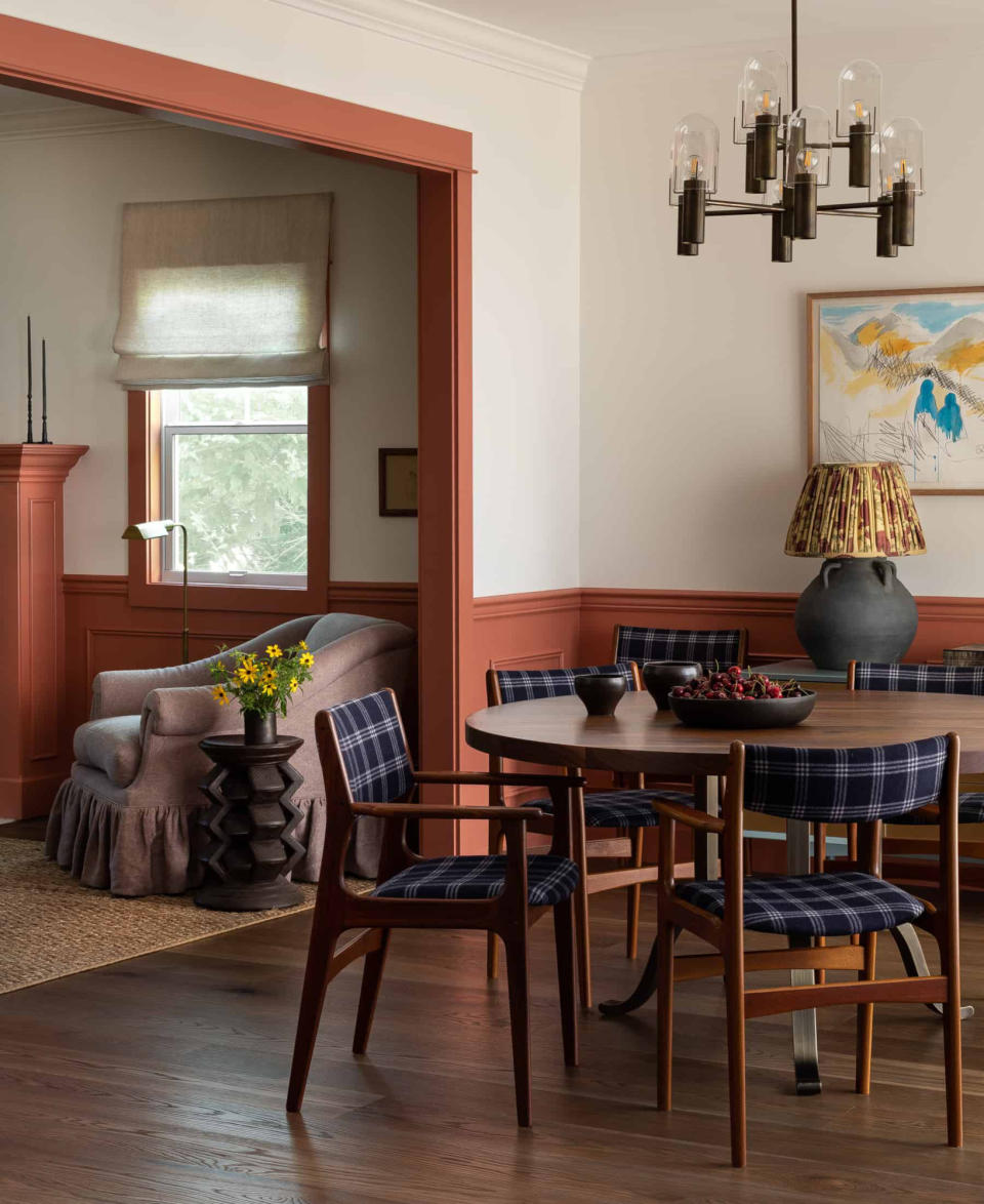 Broken plan living-dining room with dark wood flooring, dark wood round table and chairs, and panelling and woodwork painted in terracotta
