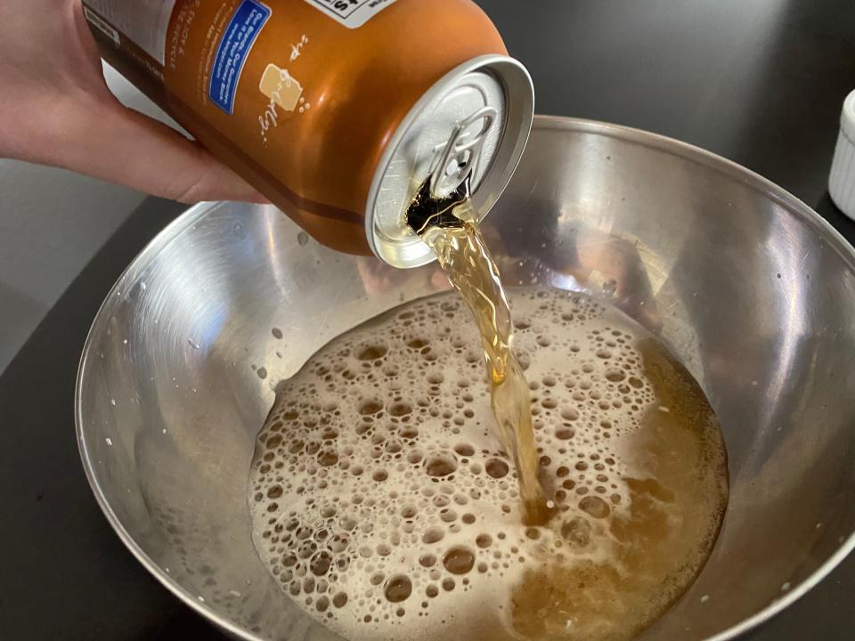 hand pouring soda into a metal mixing bowl