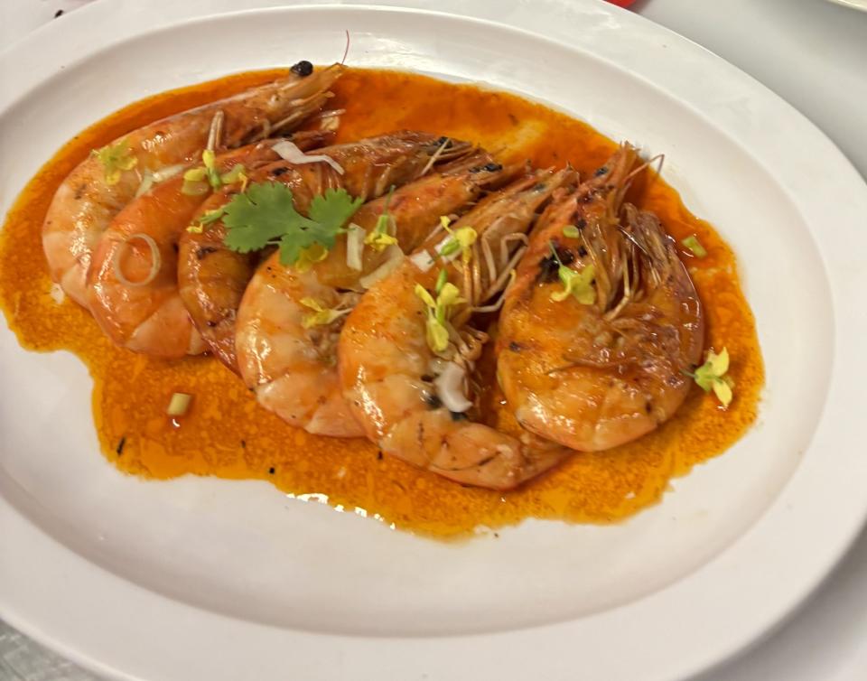 A student plates a dish of local whole shrimp in a pan sauce and topped with fresh herbs and edible flowers.