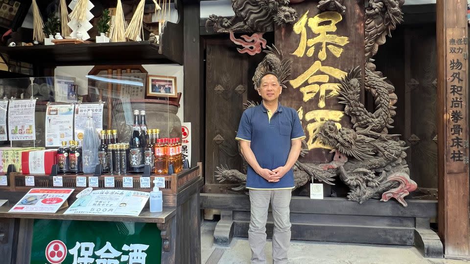 Sixth-generation brewer Ryochi Okamoto stands in front of a dragon signboard from the village's first homeishu brewer. - Beth Reiber