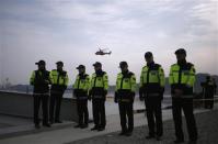 Police officers are seen as a rescue and salvage team helicopter (top) flies over a port where family members of missing passengers from the capsized passenger ship Sewol gathered to wait for news from rescue and salvage teams, in Jindo April 22, 2014. REUTERS/Kim Hong-Ji