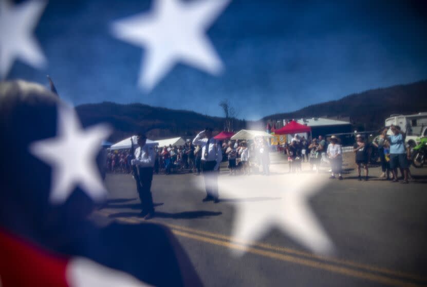 Greenville, CA - July 16: The start of Greenville's Gold Diggers Day parade celebration is visible through an American flag on Saturday, July 16, 2022, in Greenville, CA. The Greenville community gather for their traditional parade even after the Dixie Fire that greatly impacted their town nearly one year ago. (Francine Orr / Los Angeles Times)