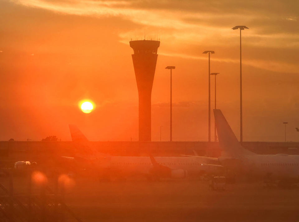 Airport tarmac at sunset with airplanes parked and a visible control tower in the background