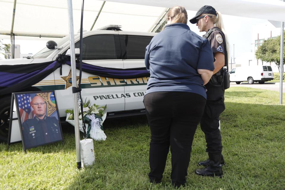 Shannon McDonald, Pinellas County Schools Police communications center supervisor, middle, and Barbara Baugher, K-9 officer, share a moment together near a make-shift memorial for Deputy Michael Hartwick, at the Pinellas County Sheriff's Office headquarters on Friday, Sept. 23, 2022, in Largo, Fla. Hartwick, a Florida sheriff's deputy working an overnight shift to provide safety at a construction zone was struck and killed by a worker operating a front end loader, officials said.(Jefferee Woo/Tampa Bay Times via AP)