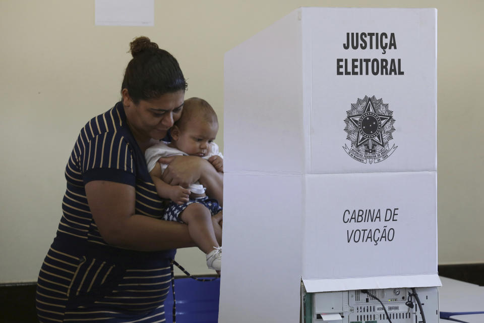 A woman cradles her baby while casting her vote at a polling station in a suburb of Brasilia, Brazil, Sunday, Oct. 28, 2018. Jair Bolsonaro, presidential candidate with the Social Liberal Party, is running against leftist candidate Fernando Haddad of the Workers’ Party. (AP Photo/Eraldo Peres)