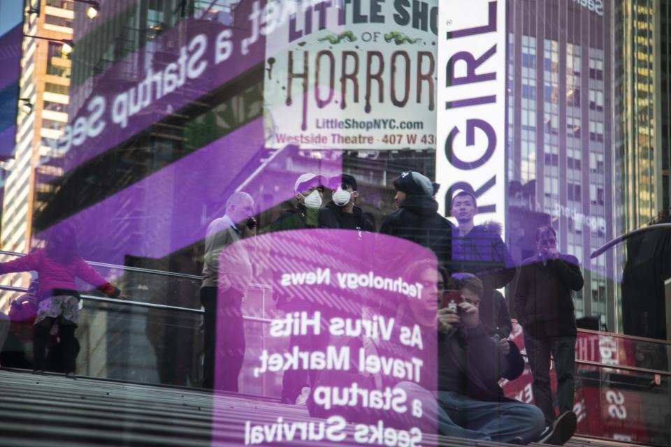 Tourists wear face masks as news about the coronavirus is seen in a reflection off a glass surface in Times Square in New York on Sunday, March 15, 2020. President Donald Trump on Sunday called on Americans to cease hoarding groceries and other supplies, while one of the nation's most senior public health officials called on the nation to act with more urgency to safeguard their health as the coronavirus outbreak continued to spread across the United States. (AP Photo/Wong Maye-E)