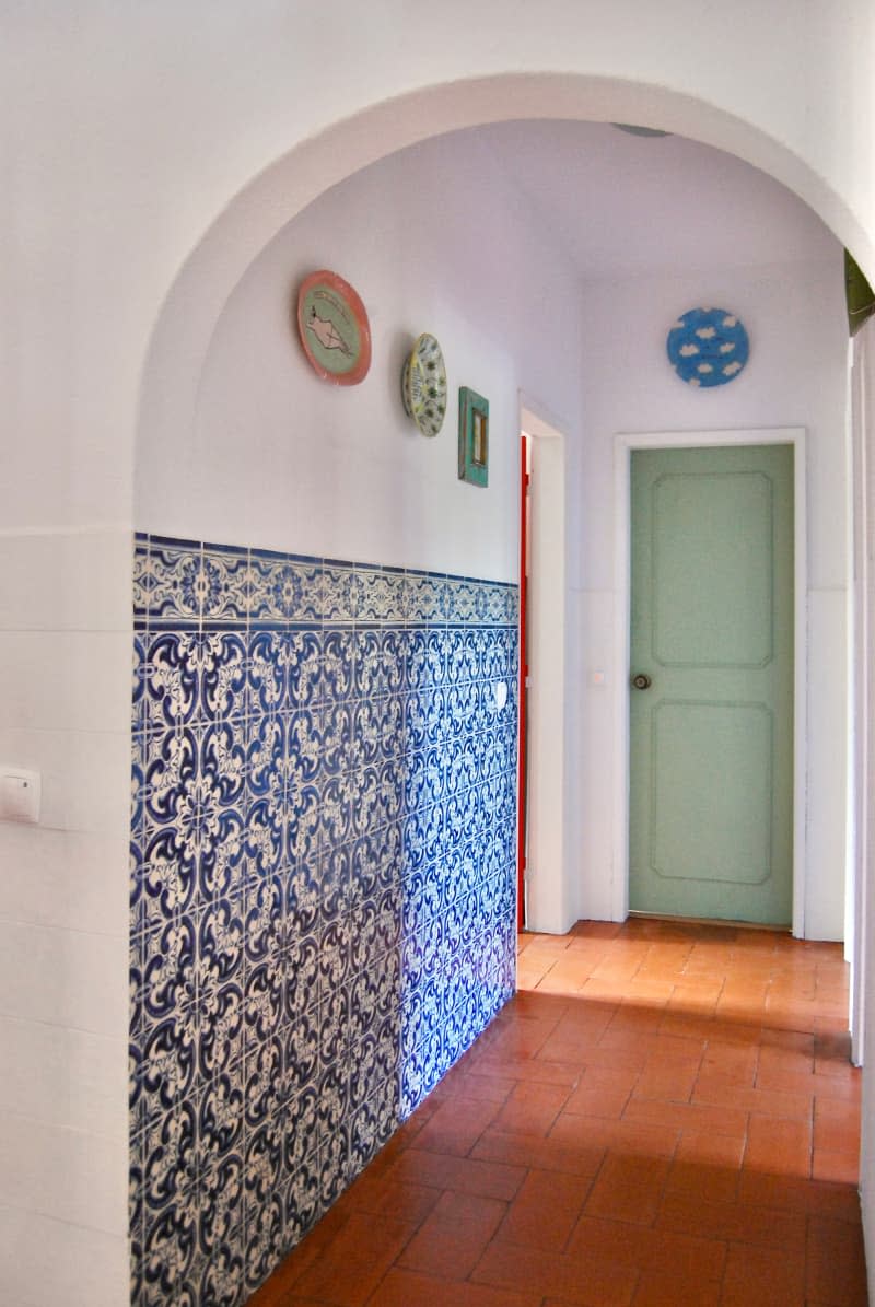 Mint green door in hallway with blue tiled wall and rust floor.