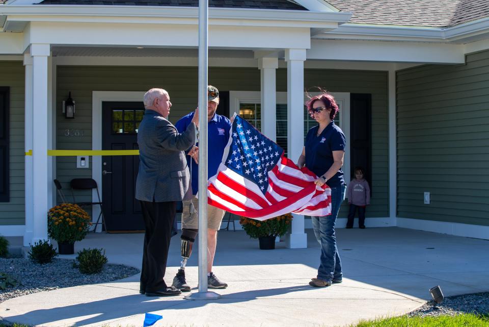 Tom Landwermeyer, the CEO of Homes for Our Troops, Marine LCpl. Bryan Chambers and his wife, Rhyann Chambers, raise the American flag over Chambers' new home, on Saturday, Oct. 1, 2022, in Attica, Ind.