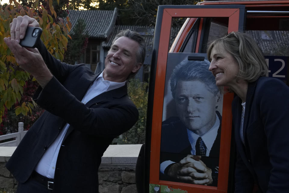 California Gov. Gavin Newsom, left, takes a selfie with a commemorative cable car carriage featuring former U.S. President Bill Clinton during a visit to the Mutianyu Great Wall on the outskirts of Beijing, Thursday, Oct. 26, 2023. Newsom is on a weeklong tour of China to push for climate cooperation. (AP Photo/Ng Han Guan)