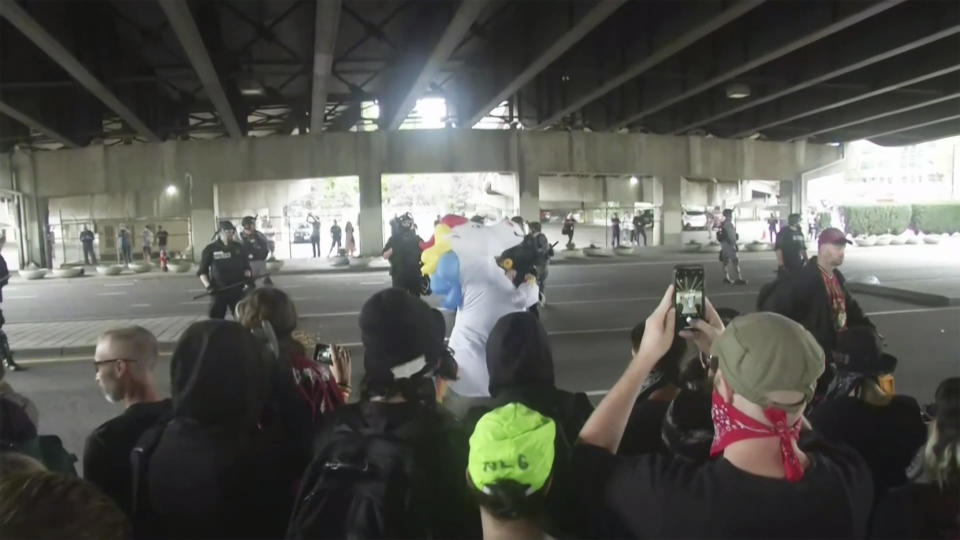 Portland police riot gear watch counterprotesters gathered in downtown Portland, Ore., on Saturday, Aug. 17, 2019. Police seized weapons such as bear spray and shields as right-wing groups and counterprotesters gathered on Saturday. Authorities also set up concrete barriers and closed streets in an effort to contain the groups. (AP Photo/APTN)