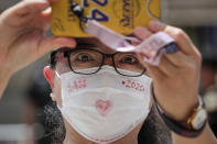 A woman wearing a face mask to protect against the new coronavirus films students leave the school after finishing the first day of China's national college entrance examinations, known as the gaokao, in Beijing, Tuesday, July 7, 2020. China's college entrance exams began in Beijing on Tuesday after being delayed by a month due to the coronavirus outbreak. (AP Photo/Andy Wong)