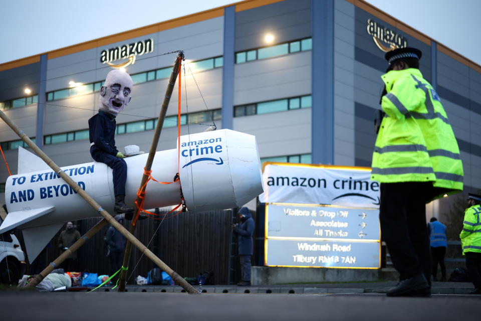 A person wearing a head mask depicting Amazon founder, Jeff Bezos sits on a fake rocket as Extinction Rebellion activists block an entrance to an Amazon fulfilment centre in Tilbury, Essex, Britain, November 26, 2021. REUTERS/Henry Nicholls