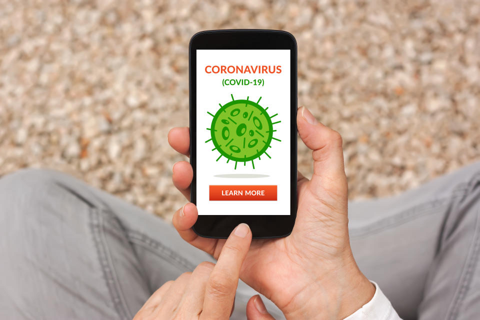 Hands holding smart phone with coronavirus, covid-19 concept on screen. Social distancing. Top view