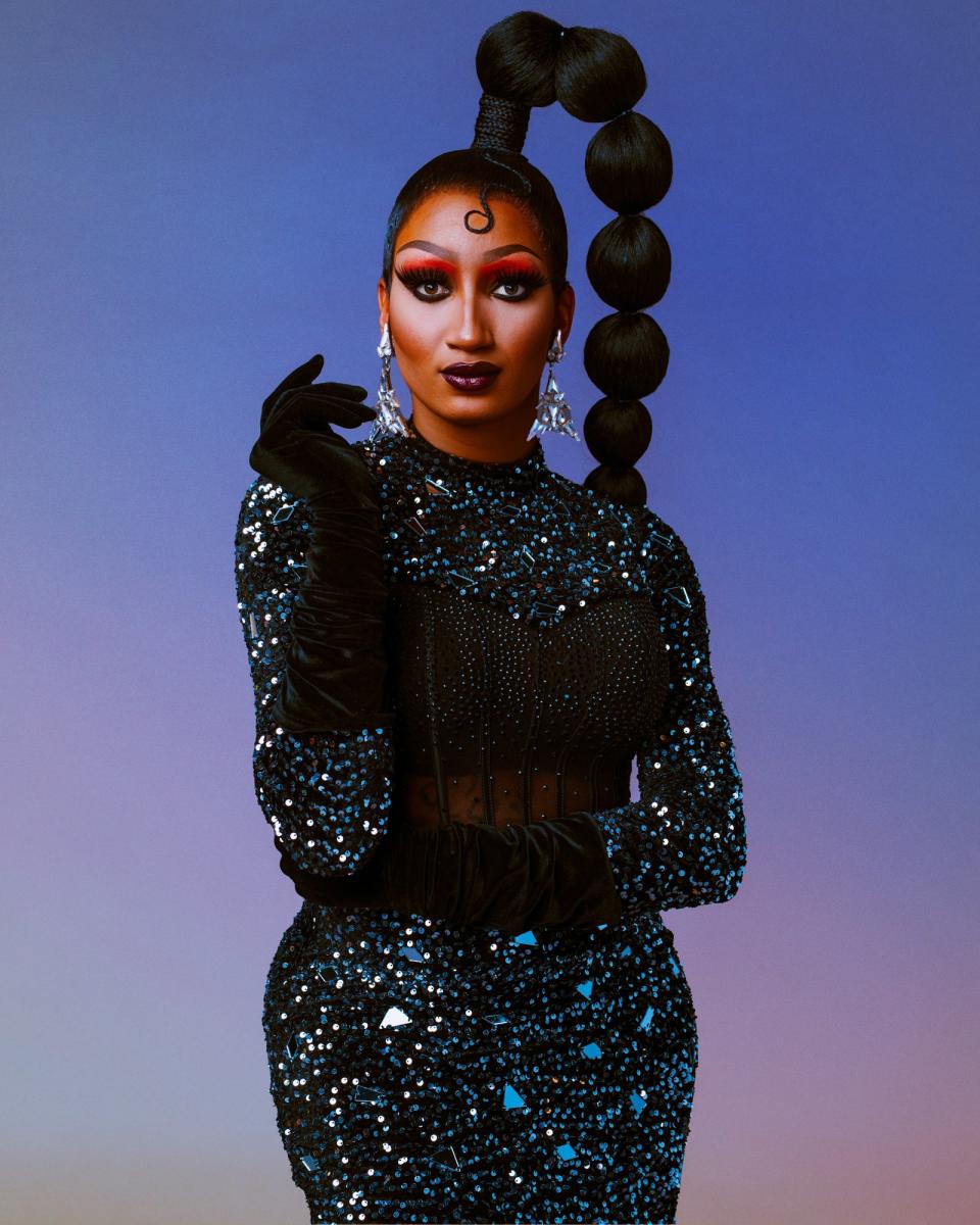 Angeria Paris VanMichaels is posing in a sequined gown with long, black gloves, dramatic makeup, and a braided hairstyle with large, spherical sections