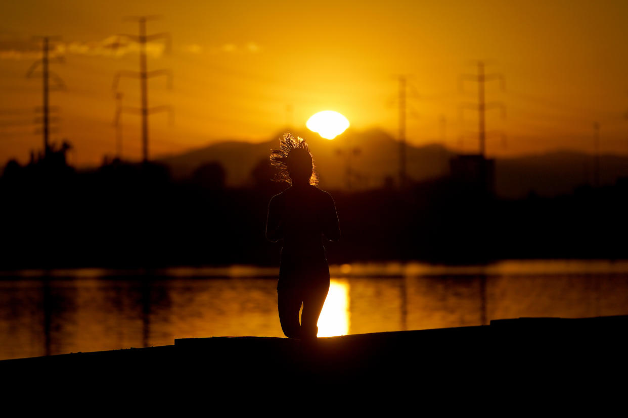 A runner jogs along a lake at sunrise.