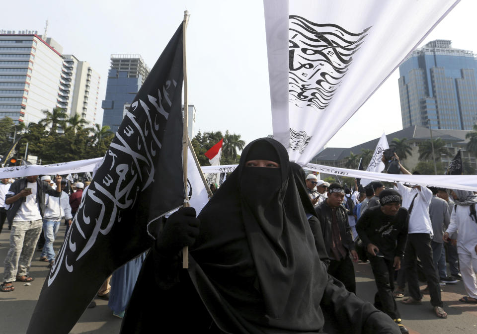 A Muslim woman holds a flag with Arabic writings that read: "There's no god but Allah and Muhammad is his messenger" popularly known as "'tauhid flag" which is often linked with banned Islamic group Hizbut Tahir Indonesia, during a protest in Jakarta, Indonesia, Friday, Nov. 2, 2018. Thousands of conservative Muslims staged the protest in the capital against the burning of the flag by members of Nahdlatul Ulama, the country's largest mainstream religious organization. (AP Photo/Achmad Ibrahim)