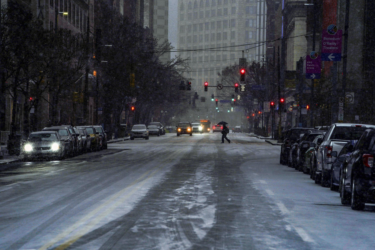 A pedestrian uses an umbrella as they cross Liberty Avenue, in downtown Pittsburgh, as snow begins to fall during a winter storm that will impact the region on Sunday night, Jan. 16, 2022. (Alexandra Wimley/Pittsburgh Post-Gazette via AP)