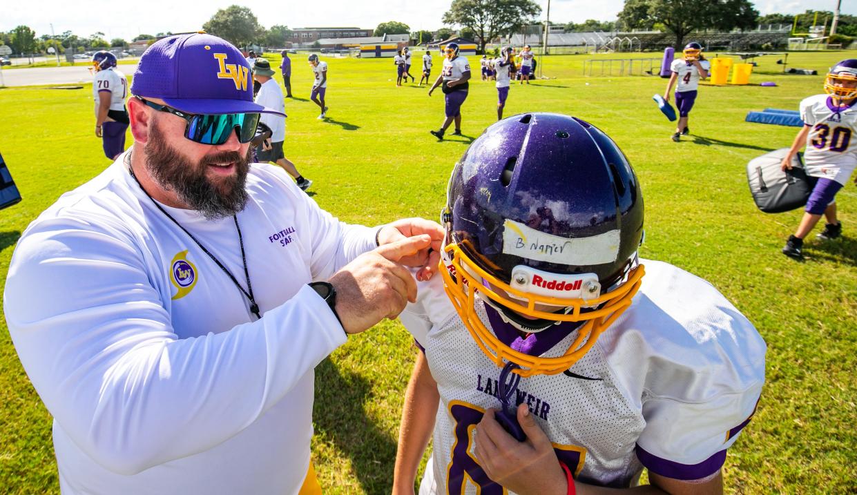 Lake Weir High School Head Football Coach Eoghan Cullen helps a player with his chin strap during football practice August 11, 2021.