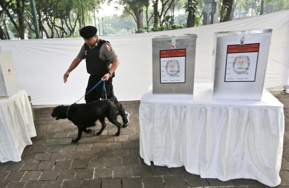 A police officer leads a bomb-sniffing dog past ballot boxes as they conduct a security sweep at a polling station near where Indonesian presidential candidate Joko Widodo will cast his vote in Jakarta, Indonesia, Wednesday, July 9, 2014. (AP Photo/Dita Alangkara)