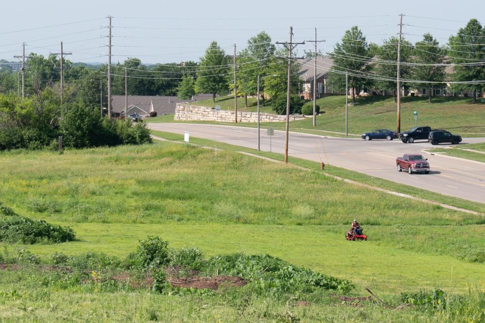 Traffic passes on S.W. Gage Boulevard on Tuesday as a man mows grass in the general vicinity where a planned Elevation Parkway is to be constructed.