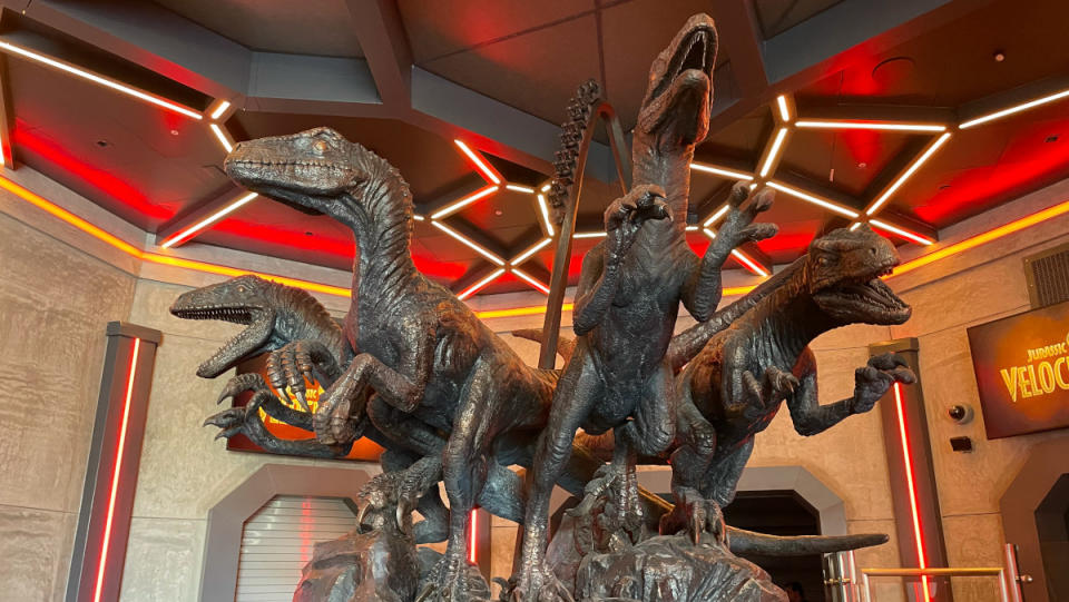 Statues of raptors leaping out from the VelociCoaster queue