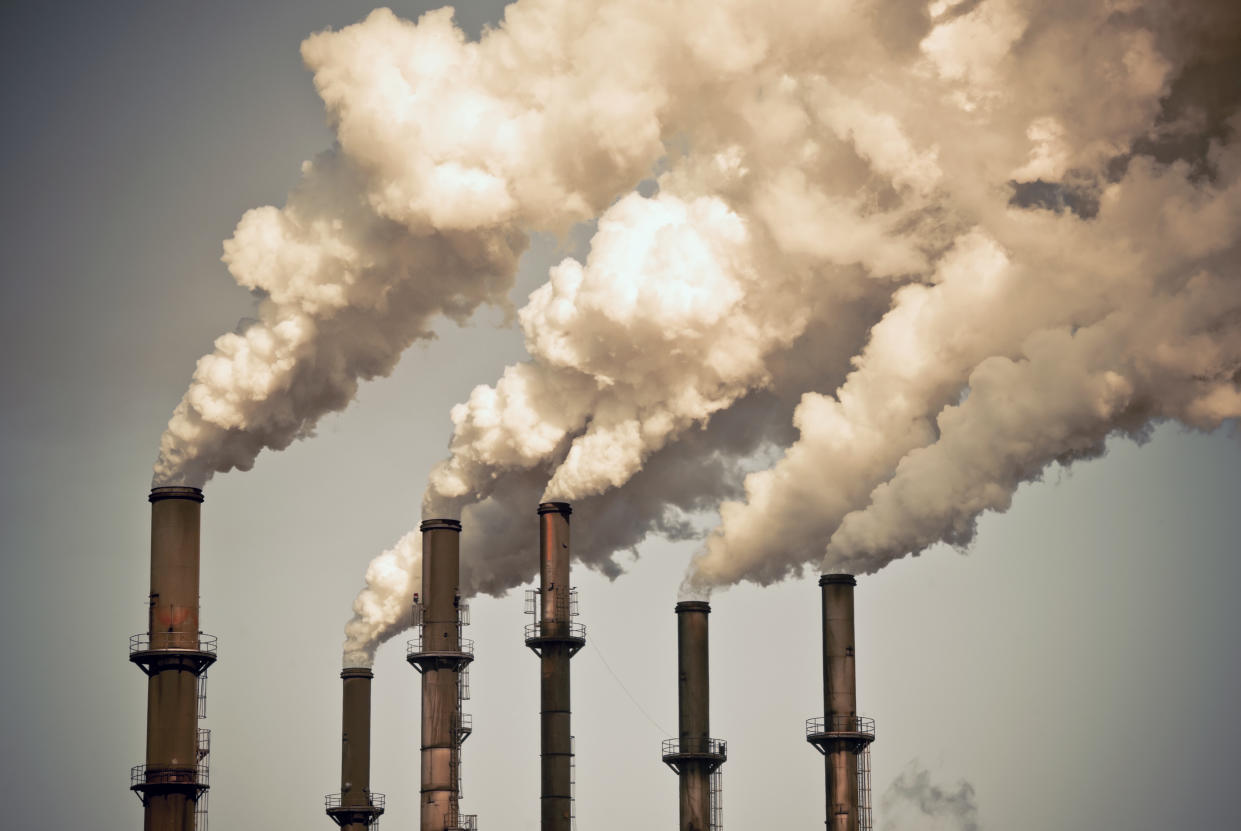 A photo of six industrial smokestacks with smoke coming out.