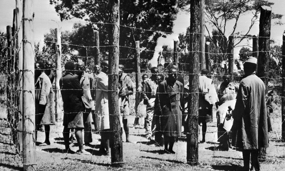 In October 1952 soldiers guard suspected Mau Mau fighters behind barbed wire in the Kikuyu reserve in Kenya.