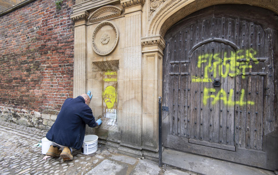 A man tries to remove a spray painted writing "Eugenics is genocide. Fisher must fall" on Ronald Fisher, founder of the Cambridge Eugenics society, by activists on the Gate of Honor, of Cambridge University, in Cambridge, Britain, Friday, June 12, 2020, following Black Lives Matter protests that took place across the UK over the weekend. The protests were ignited by the death of George Floyd, who died after he was restrained by Minneapolis police on May 25. (Aaron Chown/PA via AP)