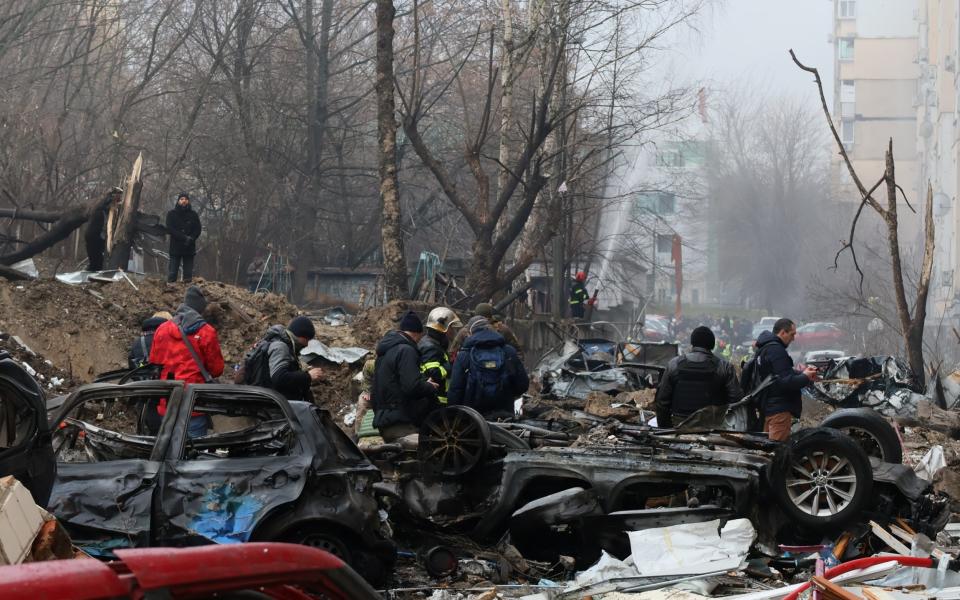 Survivors stand among destroyed cars in the yard of a damaged residential building