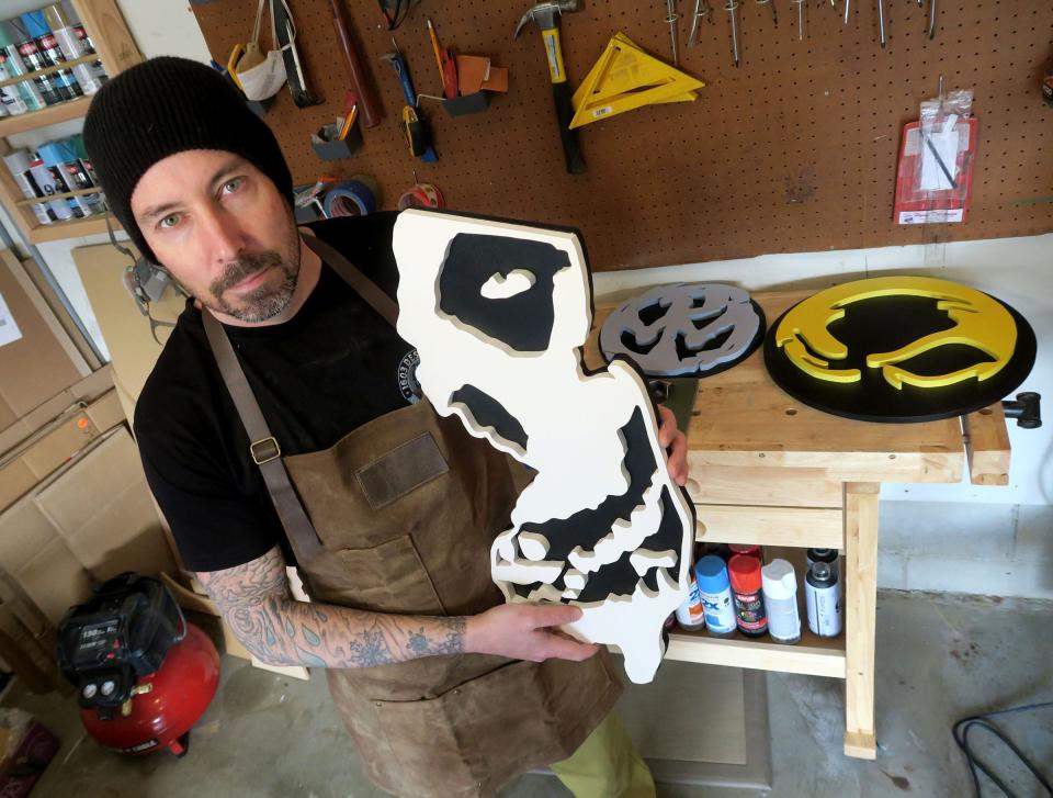 1603 Designs owner Jeff Small holds a sign he created for the "Misfits" in his shop in the garage of his Brick Township home Monday, April 3, 2023.  The two-year-old Brick-based provider of carved wooden logos.